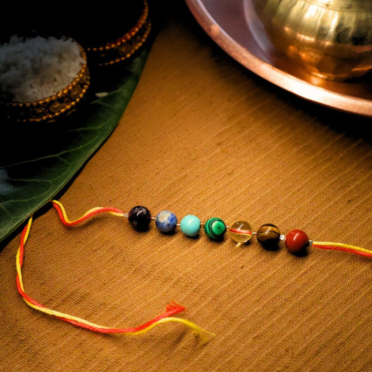 7 Chakra Rakhi made with healing crystals – Red Jasper, Tiger Eye, Citrine, Malachite, Turquoise, Lapis Lazuli, and Amethyst – arranged on a thread for brother’s protection and positive energy